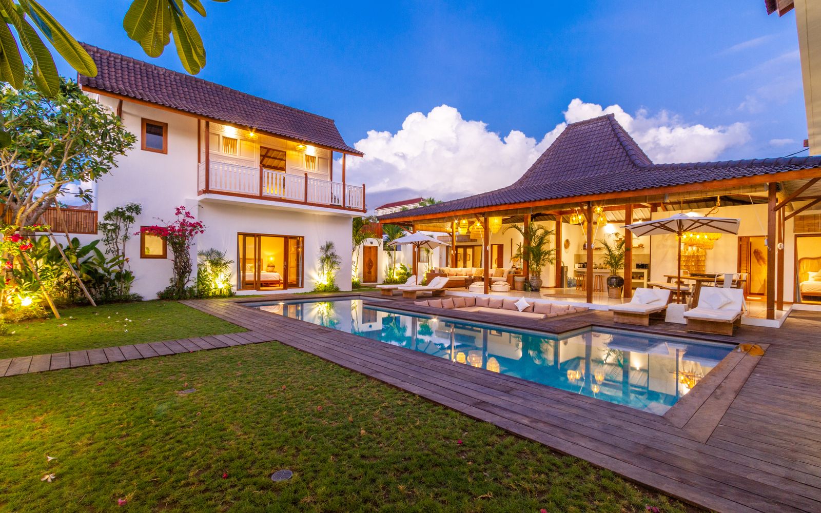 Stunning tropical villa exterior featuring a pool, wooden deck, and lush garden under a blue sky.