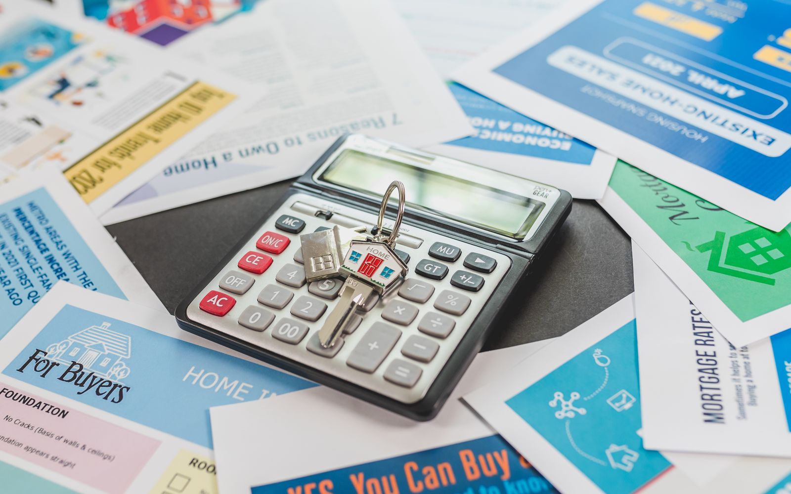 A calculator and real estate flyers depicting financial planning for home buyers.